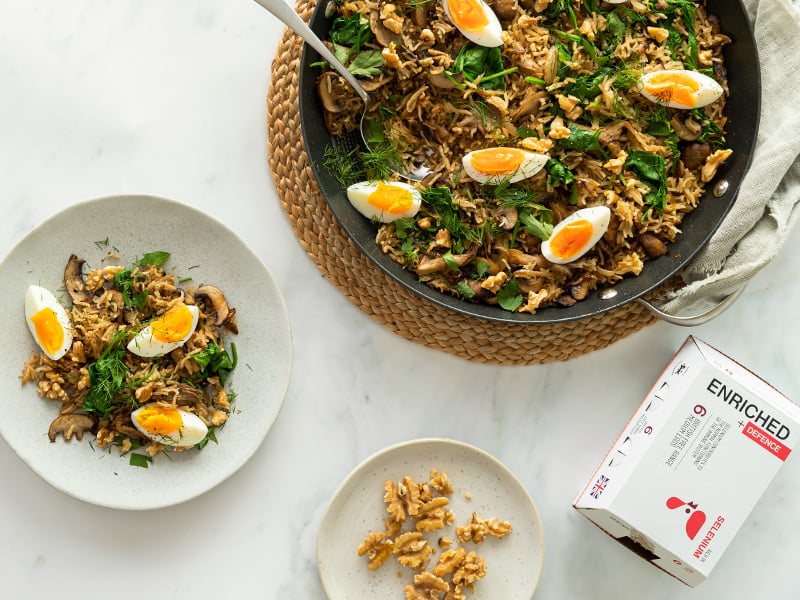 A large pan of mushroom pilaf next to a plate of pilaf and box of Enriched Eggs.
