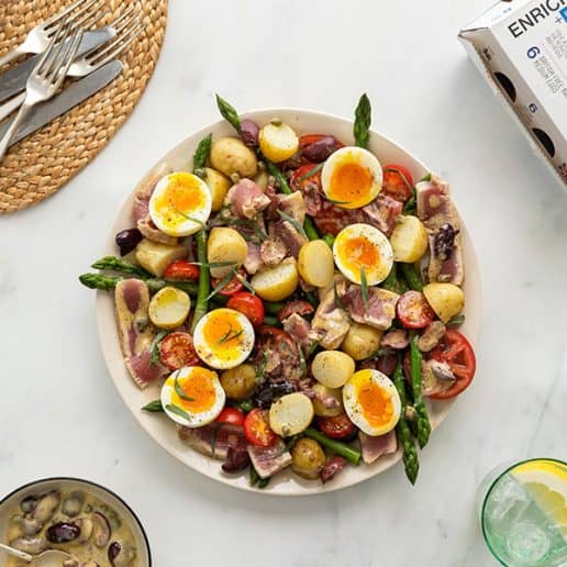 Tuna Niçoise salad on a large platter surrounded by glasses of water, cutlery and a white box of Enriched Eggs