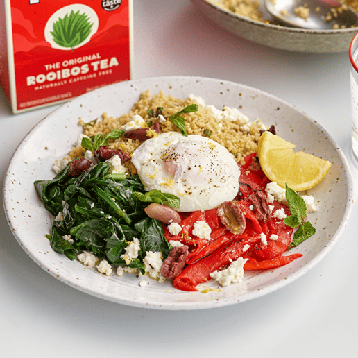 Poached egg sits on top of a bowl of chopped vegetables and lemon wedge, in front of a red box of Tick Tock Original Rooibos tea and glass of water